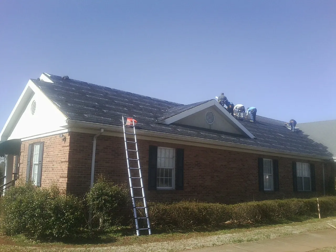 Crew tearing shingles off a brick ranch roof with a ladder set — Emergency Roof Repair work by our crew in Buckeye Lake