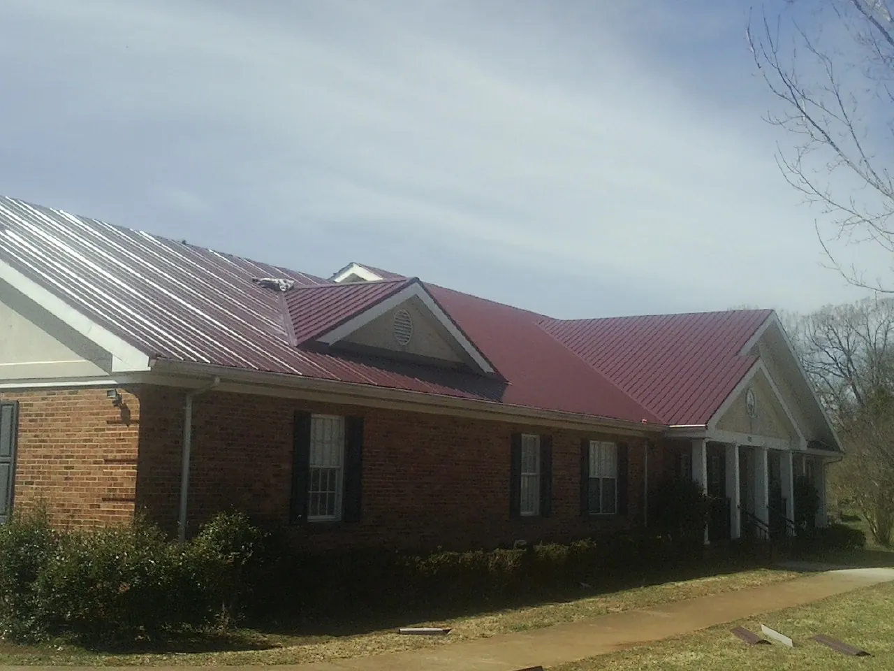 Red metal roof with gabled entries on a long brick building, from a Hail Damage Roof Repair job in Buckeye Lake