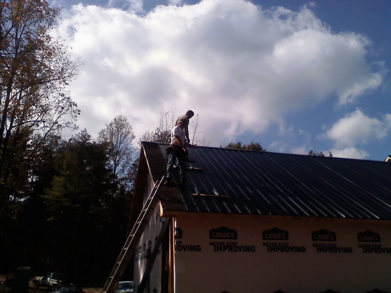 Roofer fastening dark metal panels high against a cloudy sky, from a Roof Inspection job in Buckeye Lake