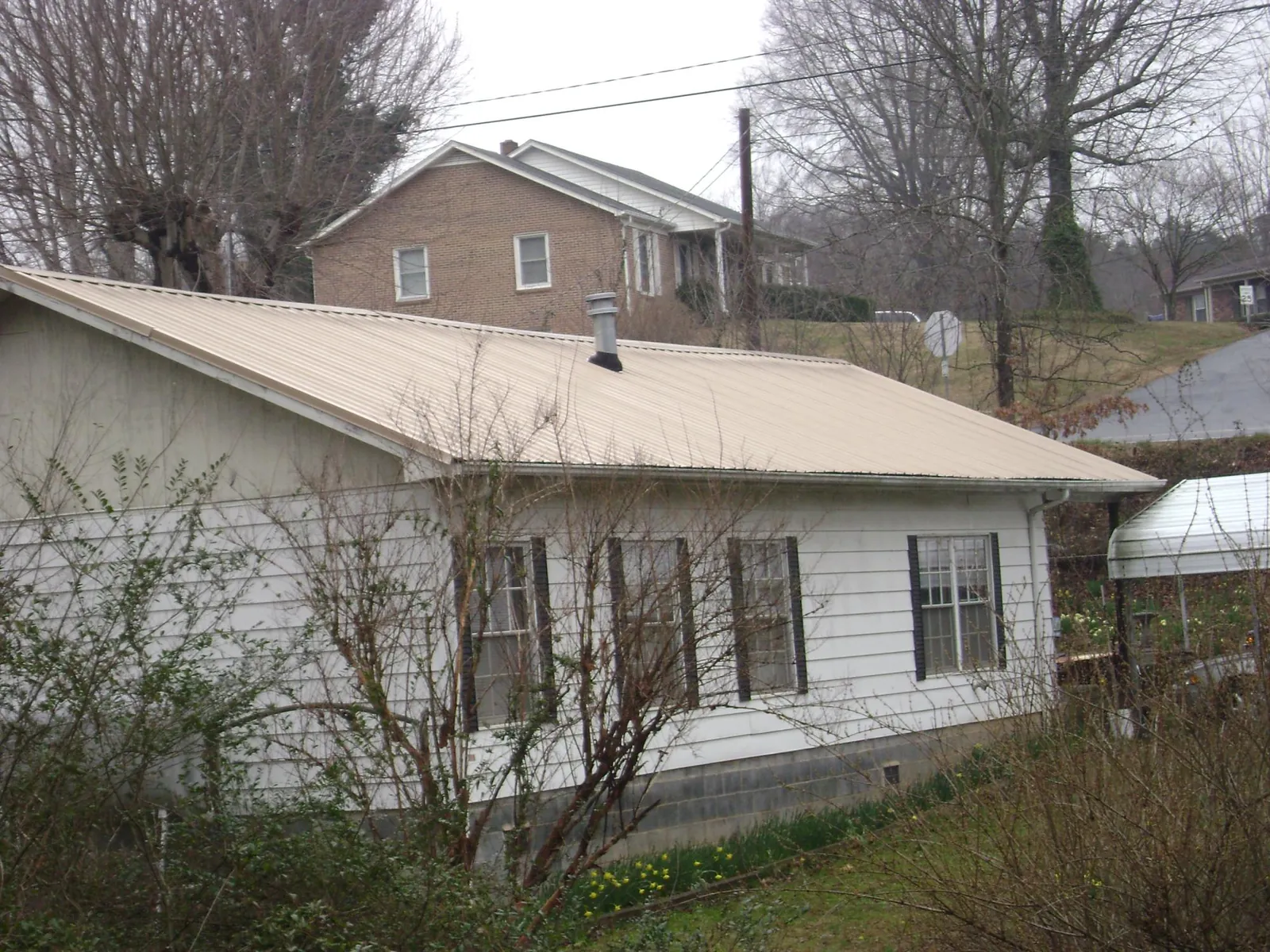Tan metal roof on a white sided house set into a hillside — Commercial Roofing by Roofing Brothers in Buckeye Lake