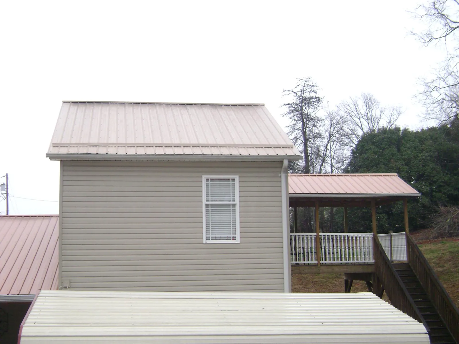 Tan metal roofs on a two story addition and attached porch, from a Roof Replacement job in Buckeye Lake